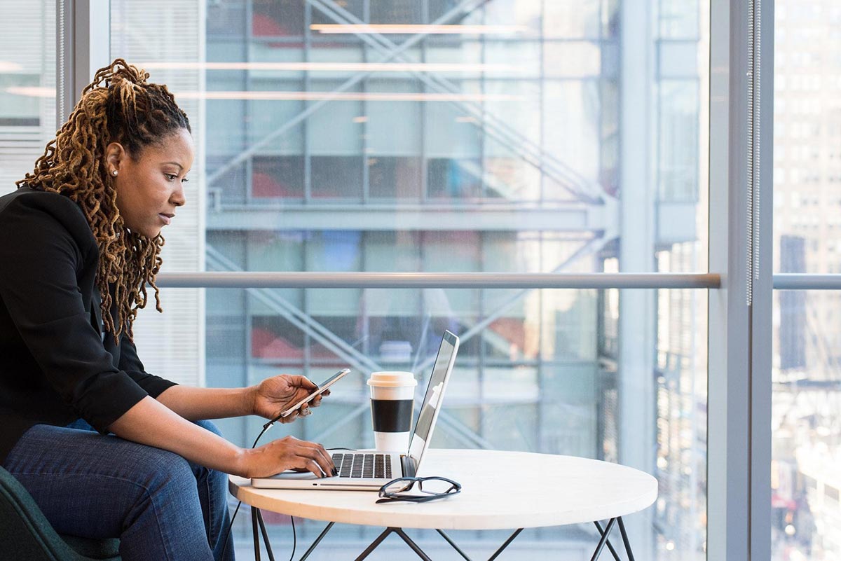 woman holding smartphone sitting in front of laptop